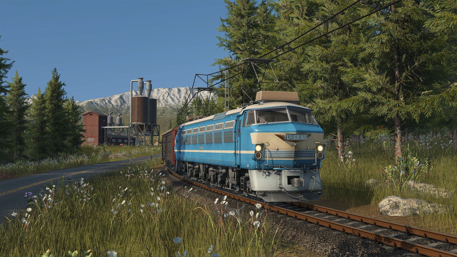 Transport Fever 3 screenshot: a blue electric locomotive pulling freight past an industrial site